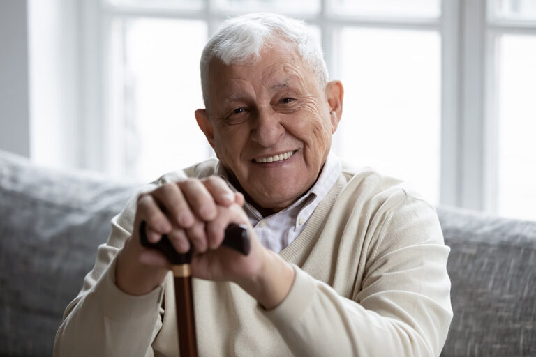 Portrait of happy senior grandfather sitting on couch looking at camera demonstrating white healthy teeth in smile. Satisfied elderly man patient having healthy habit of regular visiting dental clinic